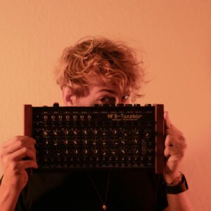 A young man holding an analogue drum machine against a warm background.