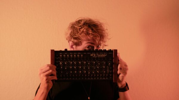 A young man holding an analogue drum machine against a warm background.