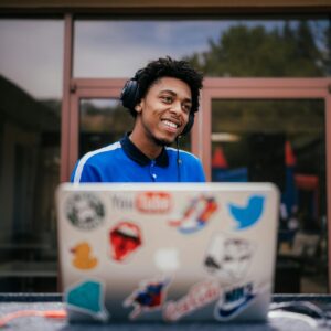 Young disc jockey in blue shirt smiling while mixing music on a laptop outdoors.