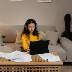 Young girl studying music with a laptop in a cozy living room setting.